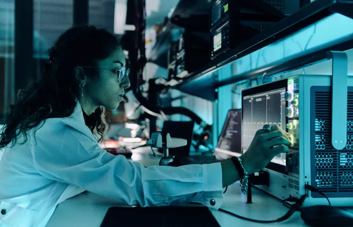 A student in a lab coat operates electronic testing equipment in a high-tech laboratory setting.